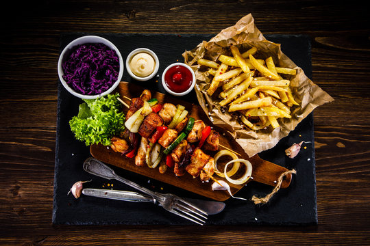 Kebabs - grilled meat with french fries and vegetables on wooden background 