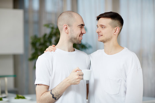 Two amorous gay men looking at one another while one of them having coffee in the morning