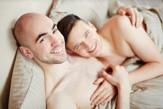 Young affectionate smiling gay men lying in bed and looking at camera