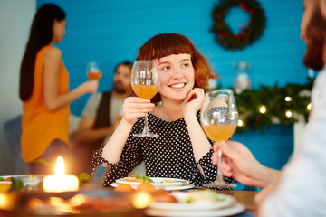 Happy girl toasting with glass of juice while looking at her boyfriend by dinner