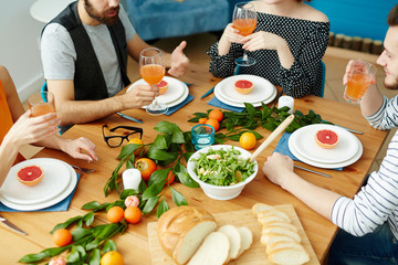 Group of vegetarians sitting by festive table with healthy food and having talk