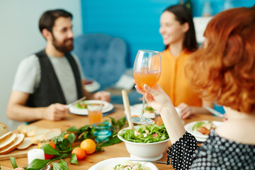 One of girls holding glass of juice in hand while sitting by festive table among her friends