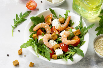 Festive appetizer. Salad with shrimps, feta cheese, arugula, cherry tomato and sesame on a stone or slate background.