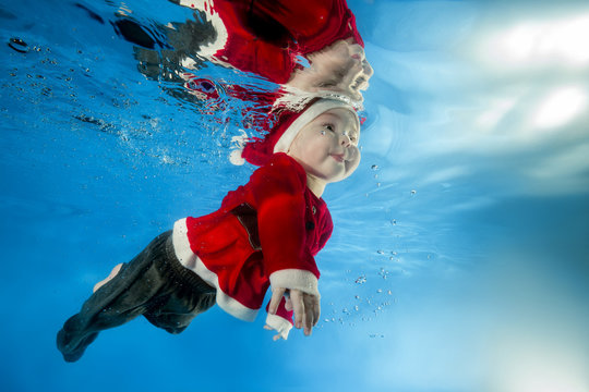 A little boy in Santa's cost swims underwater in the pool