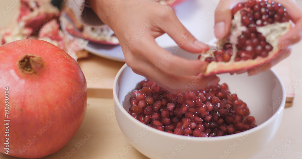 Poster Putting Fresh red pomegranate into bowl