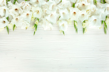 Flowers texture made of white gladioluses on wooden white background. Pattern of gladioli with space for your text holiday greeting card. Lay Flat, top view. Flowers texture. Frame of flowers.
