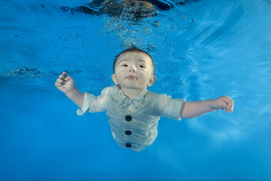 little boy in a costume swims underwater in the pool
