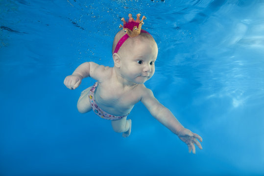 A little girl in a crown swims underwater in the pool