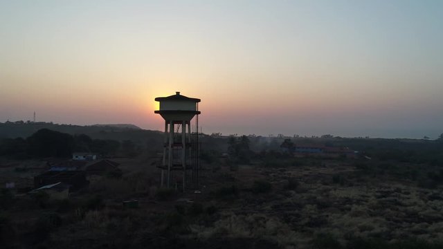Flying around a water tower in a small Indian village in the beautiful sunset. Aerial view.