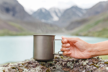 A girl drinks a fragrant herbal tea near a mountain lake on a hike
