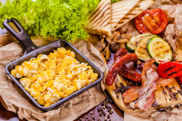 English breakfast with scrambled eggs, sausages, bacon, vegetables and spices