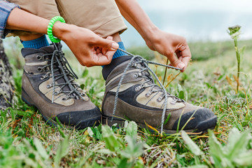 a tourist woman ties up her shoelaces on trekking boots, outdoor footwear concept