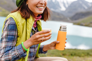 Traveler girl pouring tea from thermos during hike in mountains