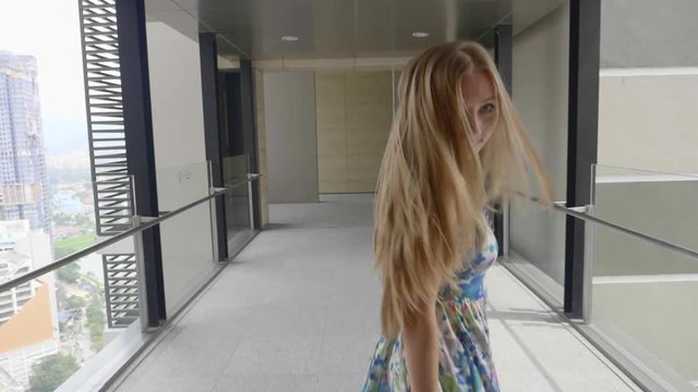 Beautiful blonde girl with healthy long hair outdoors. Happy smiling young woman enjoying vacation, having fun and spinning in the hall. Happiness, freedom concept. Slow motion.