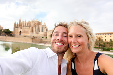 Happy couple in love taking selfie photo with phone on summer vacation in front of the Palma Cathedral, La Seu, in Palma, Majorca, Spain. Europe travel holidays people having fun.