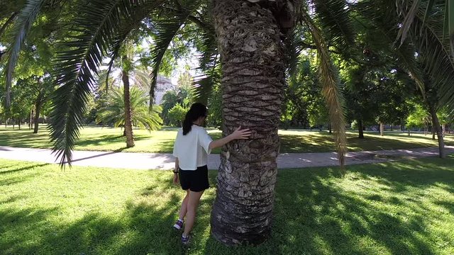 Young Caucasian Woman Walking On Green Grass Around Palm Trees in Garden Of Turia River Park, Valencia, Spain, Europe, Oct 2017