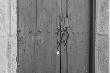 Distressed wooden double doors, with a stone frame, architectural details, and two elegant handles, in black and white 