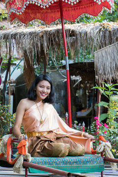 young woman in traditional Thai clothes sits on the historical litter. Thai girl in the historical costume relaxed under umbrella.