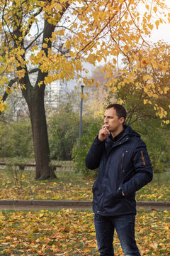Handsome man walking in the autumn park. Man smoking cigarette in outdoor. Bad habit.