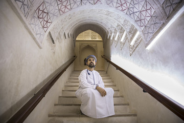 arab man in traditional omani outfit in an old castle, sitting on a staircase