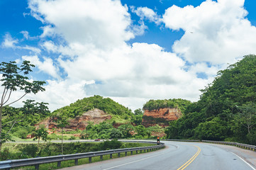 Road crossing the forest with cloudy sky and mountain view.