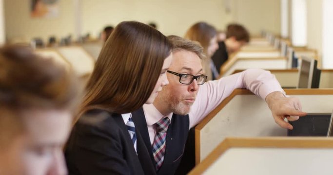 4K Caring teacher spending extra time with teen student struggling in computer class. Slow motion.