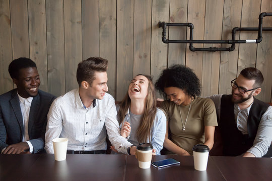 Young man joking at cafe meeting making multiracial friends laugh, diverse people guffaw after guy telling funny comic story during coffee break, happy black and white mates having fun in coffeehouse