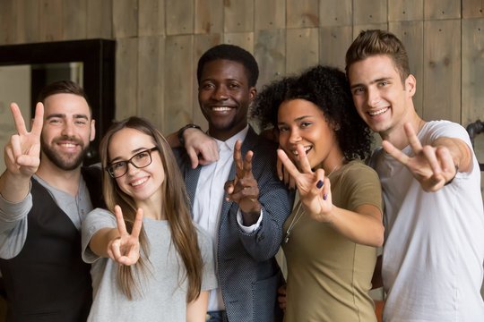 Happy multi ethnic young people looking at camera, smiling diverse friends or students showing peace sign, multicultural millennials posing together at meeting, tolerance and racial equality concept