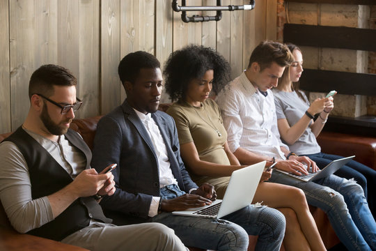 Multiracial Black And White People Sitting On Couch Ignoring Each Other Immersed In Phones And Laptops, Diverse Young Students Obsessed With Online Apps Using Modern Gadgets, Devices Overuse Concept