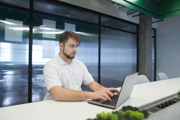 A man with a beard works at a laptop in the office. A young man enjoys a computer in a modern office.