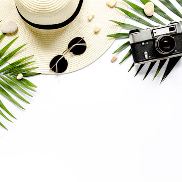 Traveler accessories, tropical palm leaf branches, camera on white background with empty space for text. Travel vacation concept. Summer background. Road frame set. Flat lay, top view.