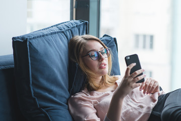 Portrait of a beautiful girl lying on the couch and using a smartphone. The girl is resting on the couch with a smartphone in her hands