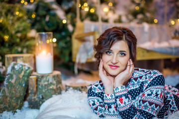 Beautiful happy girl in a sweater, on background of a Christmas tree and candle