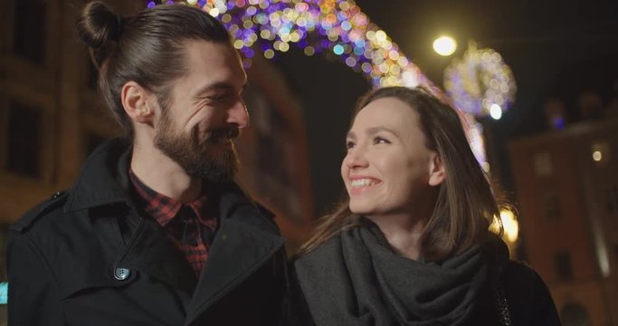 Beautiful young couple on a date standing in a city street at night, portrait.