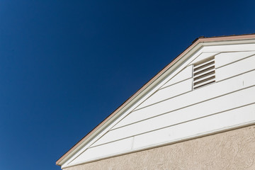 Generic house view of side and roof edge, stucco and vinyl with attic ventilation set against a deep blue sky, copy space, horizontal aspect