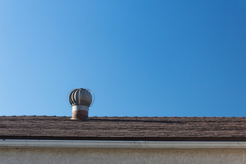 View of roof and old style spinning attic ventilator isolated against a blue sky, copy space,...