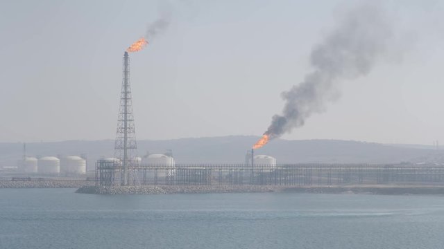 Flare stack and smoke of petrochemical refinery on sea shore in haze