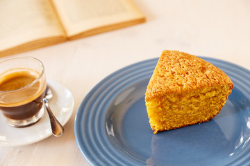 A piece of delicious carrot pie on a blue shiny plate and vintage old book. Part of a homemade cupcake on a plate with black coffee. Homemade pie on a ceramic plate on a white wooden table.