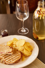 Sandwiches with cheese and sausage fried on the grill. A plate with snacks of chips and toast bread. White dish with appetizers and sauce on a brown wooden table.