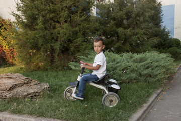 4 year old beautiful boy in a white shirt smiling on a bicycle