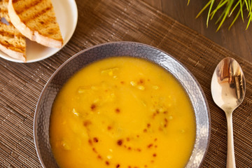Pumpkin and carrot soup on a brown wooden table. Natural ecological yellow and orange soup puree in a ceramic plate. Healthy meals for lunch with slices of toast bread.