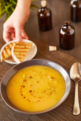Pumpkin and carrot soup on a brown wooden table. Natural ecological yellow and orange soup puree in a ceramic plate. Healthy meals for lunch with slices of toast bread.