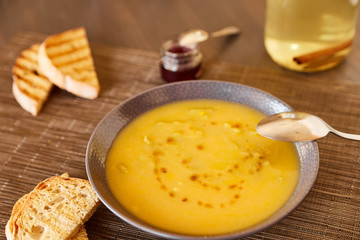 Pumpkin and carrot soup on a brown wooden table. Natural ecological yellow and orange soup puree in a ceramic plate. Healthy meals for lunch with slices of toast bread.