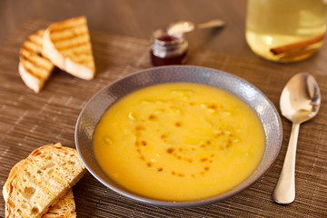Pumpkin and carrot soup on a brown wooden table. Natural ecological yellow and orange soup puree in a ceramic plate. Healthy meals for lunch with slices of toast bread.