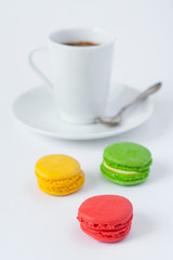 Traditional  french multicolored cakes macarons in the foreground and a cup of coffee on a saucer with spoon in a blur on a white background