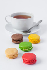 Traditional  french multicolored macarons in the foreground and a cup of tea on a saucer in a blur on a white background
