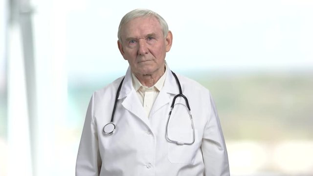 Old frown serious doctor. Touching gloomy face, bright abstract background.