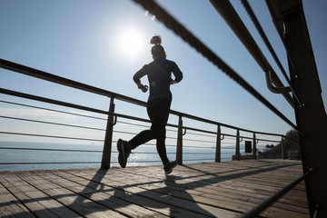 Sporty female runner running on seaside boardwalk during sunrise