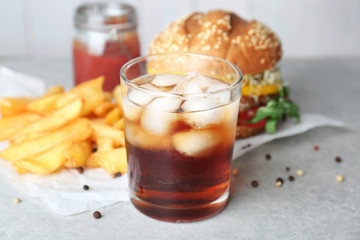 Glass of cold cola with tasty burger on table