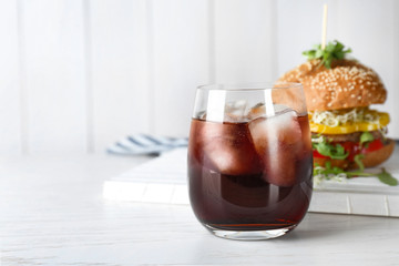 Glass of cold cola with tasty burger on table